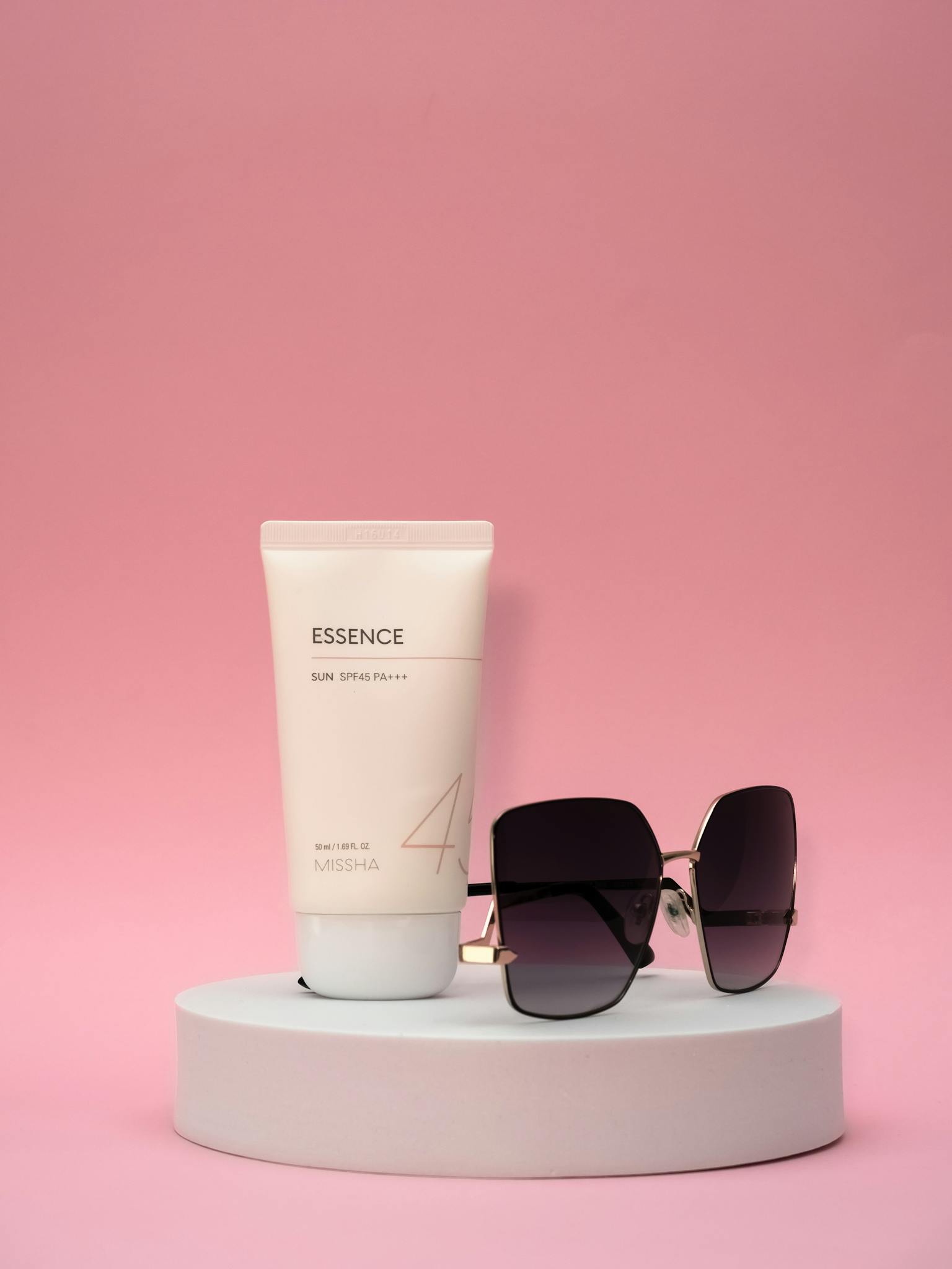 Chic skincare tube and sunglasses against a bright pink backdrop for a modern look.