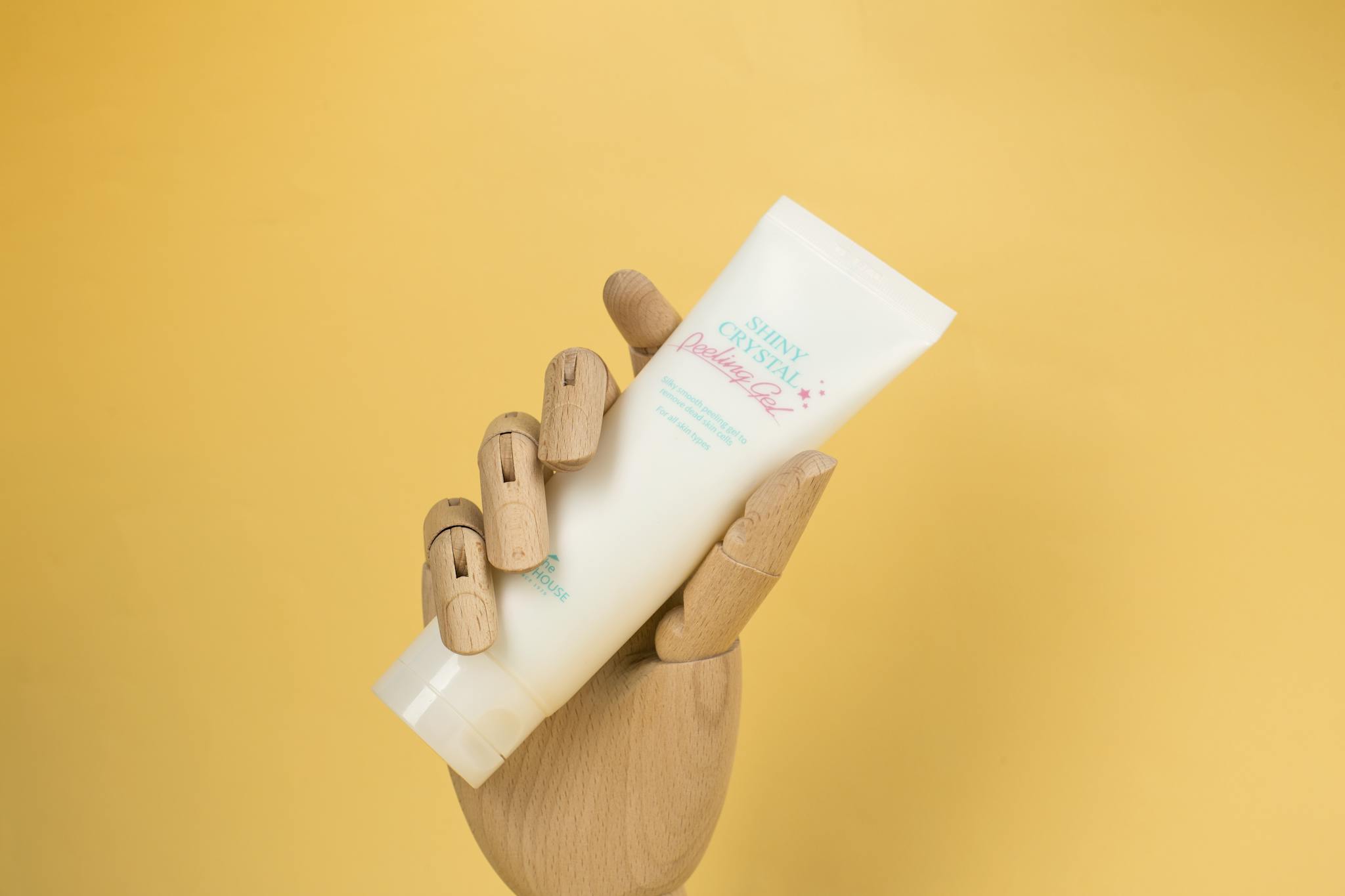 Plastic cosmetic tube held by a wooden hand against a yellow background, perfect for product mockups.